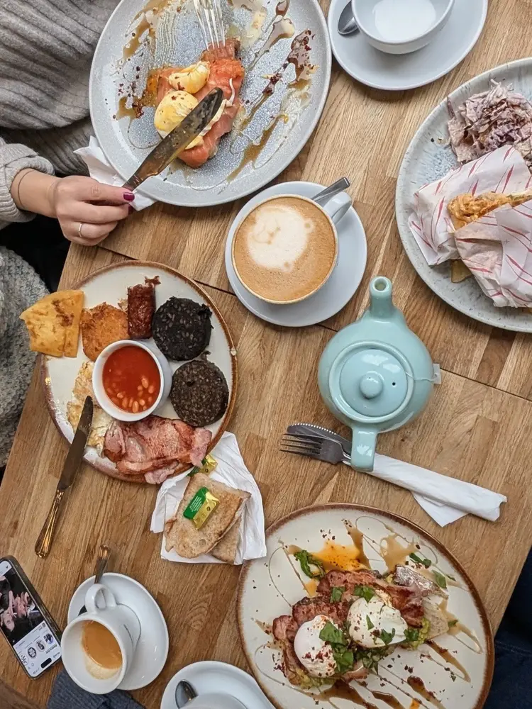 Overhead view of a shared brunch — full breakfast, salmon toast, teapot